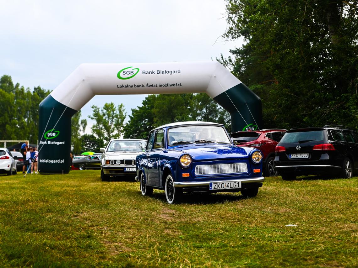 Na zdjęciu widoczny niebieski zabytkowy pojazd marki trabant, w tle różne inne pojazdy zabytkowe oraz balon sponsora Bank Spółdzielczy Białogard
