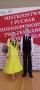  Na zdjęciu Aleksander i Kaja. Kaja ubrana w długą neonową sukienkę w odcieniu żółci z czarnymi dodatkami. Aleksander ubrany w białą koszulę z czarnym krawatem, w czarne spodnie i welurową czarną kamizelkę. Dumnie się prezentują. Na tle widać napis Mistrzostwa i Puchar Zachodniopomorskiego Związku Tańca Sportowego. 
